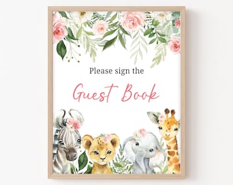 May include: A white sign with a pink floral border and a pink and white floral wreath at the top. The sign says "Please sign the Guest Book" with a pink and white floral border. There are four animals at the bottom of the sign: a zebra, a lion, an elephant, and a giraffe. All of the animals are wearing pink floral crowns.