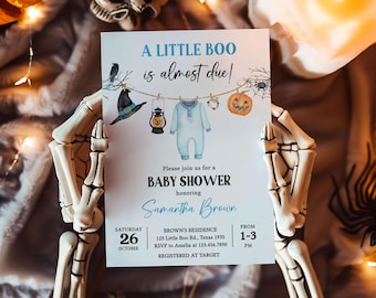 May include: A baby shower invitation with a Halloween theme. The invitation reads "A Little Boo is almost due!" and features illustrations of a witch hat, a lantern, a onesie, and a jack-o'-lantern. The invitation is held by a skeleton hand.