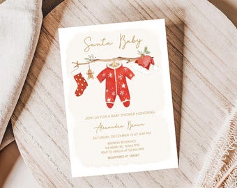 Peut inclure: Une invitation à une baby shower avec les mots "Santa Baby" en écriture dorée. L'invitation présente des illustrations à l'aquarelle d'une combinaison rouge, d'une chaussette et d'un bonnet de Père Noël. Le texte de l'invitation comprend les détails de la baby shower.