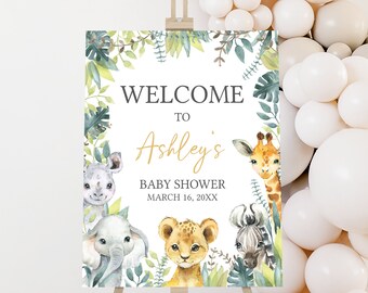 May include: Welcome to Ashley's Baby Shower sign with a jungle theme. The sign features a white background with green leaves and illustrations of a giraffe, lion, elephant, and rhinoceros. The text "Welcome to Ashley's Baby Shower March 16, 20XX" is printed in black and gold.