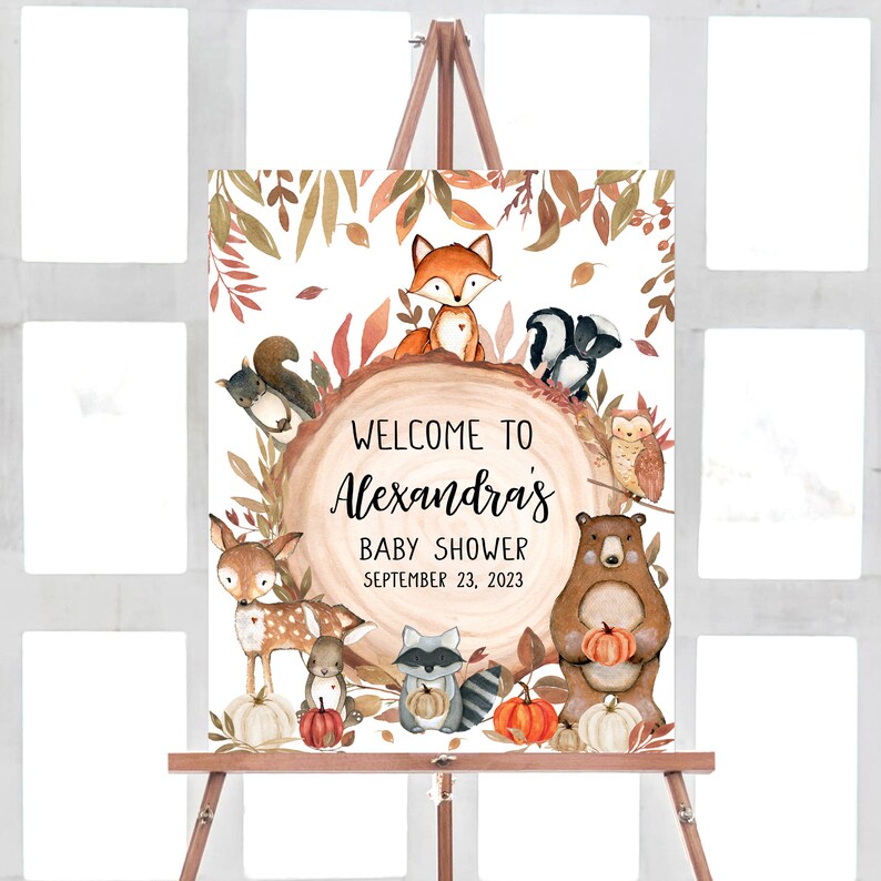 May include: A watercolor baby shower sign on a wooden easel. The sign features woodland animals, pumpkins, and fall foliage around the text "Welcome to Alexandra's Baby Shower September 23, 2023."