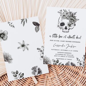 May include: Baby shower invitation featuring a skull adorned with floral elements. The invitation text reads "a little boo is almost due!" with event details. The design includes floral patterns in grayscale.