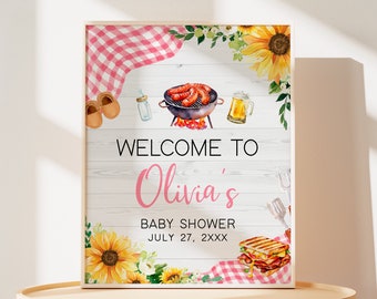 May include: Welcome to Olivia's Baby Shower sign with a white wood background, pink gingham, sunflowers, and a grill with sausages. The date is July 27, 2XXX.