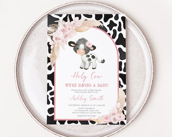 May include: A black and white cow with pink flowers on its head is featured on a baby shower invitation with a cow print background. The invitation reads "Holy Cow We're Having a Baby!" and includes the name "Ashley Smith" and details for the event.