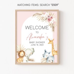 May include: A pink and white welcome sign with a brown wood frame. The sign says "Welcome to Alexandra's Baby Shower June 10, 2023". There are illustrations of a lion, elephant, rhinoceros, and giraffe.