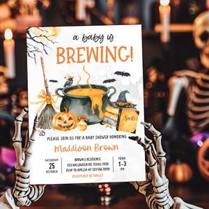 A person holding a Halloween-themed baby shower invitation with a skeleton in the background.
