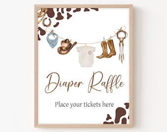 Op de afbeelding: Een wit bord met een bruin houten frame en een bruine en witte koe-print achtergrond. Het bord zegt "Diaper Raffle" in bruin cursief schrift en "Place your tickets here" in bruine tekst. Er hangen verschillende cowboy-thema items aan een touwtje, waaronder een cowboyhoed, laarzen, een bandana en een baby romper.