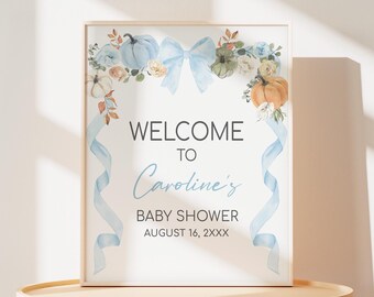 May include: A framed baby shower sign with the text "WELCOME TO Caroline's BABY SHOWER AUGUST 16, 2XXX". The sign features watercolor pumpkins, flowers, and a blue bow. Light blue ribbons cascade down the sides.