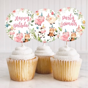May include: Three cupcakes topped with circular decorations. The decorations feature watercolor illustrations of farm animals wearing party hats, surrounded by floral wreaths. Text on the decorations reads "Happy Birthday" and "Party Animals".
