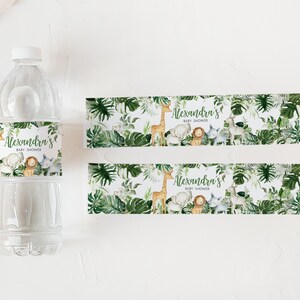 May include: Two printable water bottle labels with a jungle theme. The labels feature a giraffe, elephant, lion, and zebra with green leaves and the text "Alexandra's Baby Shower".