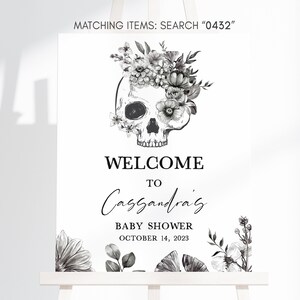 May include: A white welcome sign for a baby shower, featuring a skull adorned with floral elements. The sign reads "WELCOME TO Cassandra's BABY SHOWER OCTOBER 14, 2023". The top of the sign says "MATCHING ITEMS: SEARCH 0432".
