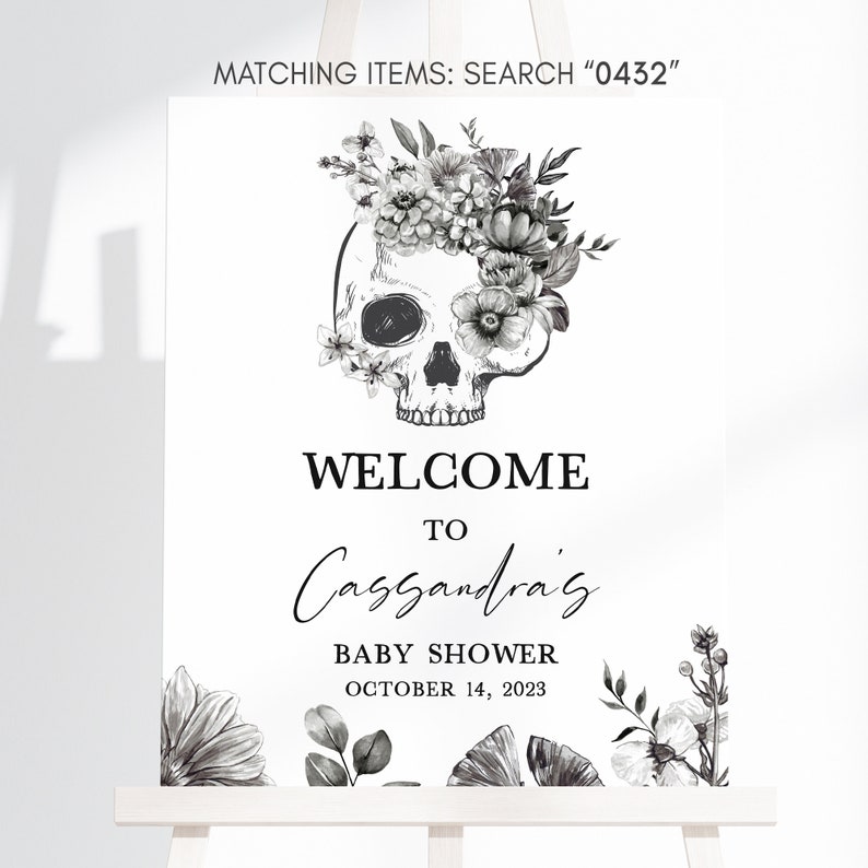 May include: A white welcome sign for a baby shower, featuring a skull adorned with floral elements. The sign reads "WELCOME TO Cassandra's BABY SHOWER OCTOBER 14, 2023". The top of the sign says "MATCHING ITEMS: SEARCH 0432".
