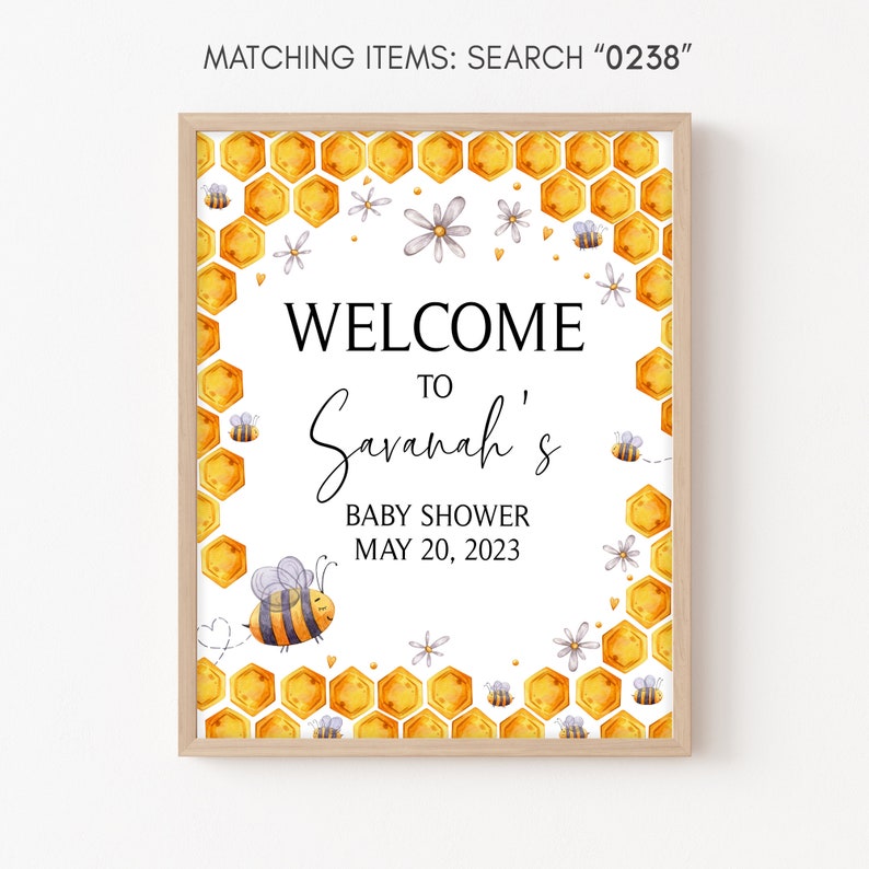 May include: A welcome sign for a baby shower with a honeycomb pattern and a bee illustration. The sign says "Welcome to Savannah's Baby Shower May 20, 2023".