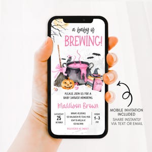 A hand holding a smartphone displaying a Halloween-themed baby shower invitation.
