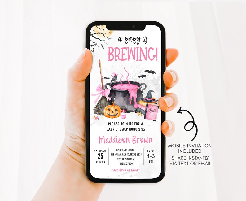 A hand holding a smartphone displaying a Halloween-themed baby shower invitation.
