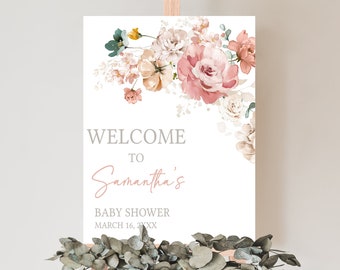 May include: A white welcome sign on an easel, adorned with a floral arrangement in shades of pink, peach, and cream. The sign reads "WELCOME TO Samantha's BABY SHOWER MARCH 16, 20XX". Eucalyptus garland decorates the base.