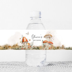 May include: Water bottle label with a watercolor illustration of mushrooms and butterflies. The text on the label reads "Olivia's Baby Shower".