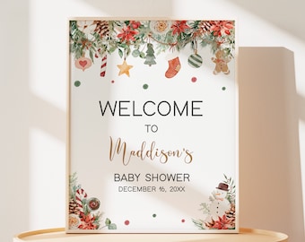 May include: A framed baby shower sign with a Christmas theme. The sign reads "Welcome to Maddison's Baby Shower December 16, 20XX." The top border features watercolor illustrations of Christmas ornaments and greenery. A snowman is in the lower right corner.
