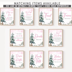 May include: A collection of framed signs with a winter theme. Each sign features a watercolor illustration of a pine tree and snowflakes on a pink background. Text on the signs includes phrases like "Mom-esa Bar" and "Diaper Raffle."