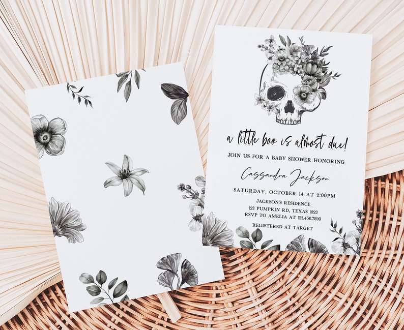 K&ouml;nnte beinhalten: Babyparty-Einladung mit einem mit Blumen geschm&uuml;ckten Totenkopf. Die Einladung lautet "a little boo is almost due!" und enth&auml;lt Veranstaltungsdetails. Das Design zeigt florale Elemente und ist auf wei&szlig;em Karton gedruckt.