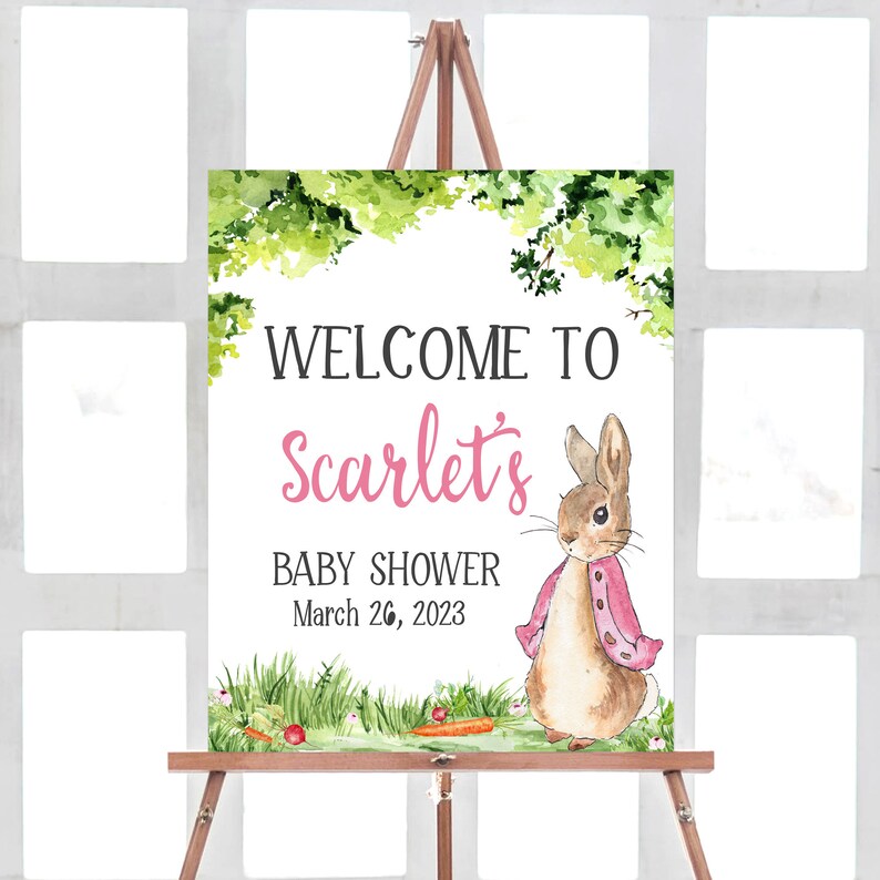 May include: Welcome to Scarlet's Baby Shower sign with a watercolor illustration of a brown rabbit wearing a pink jacket, green grass, and carrots. The date of the shower is March 26, 2023.