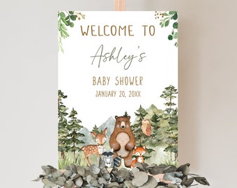May include: Welcome to Ashley's Baby Shower sign with a watercolor woodland theme. The sign features a brown bear, a deer, a raccoon, an owl, and a fox in a forest setting. The text reads "Welcome to Ashley's Baby Shower January 20, 20XX".