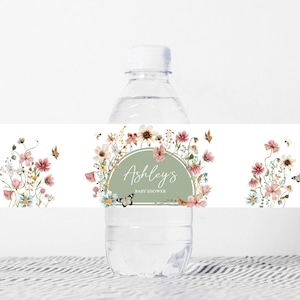 May include: Water bottle label featuring a floral design in shades of pink, green, and white. The label includes a circle with the text "Ashley's Baby Shower" in a green circle.