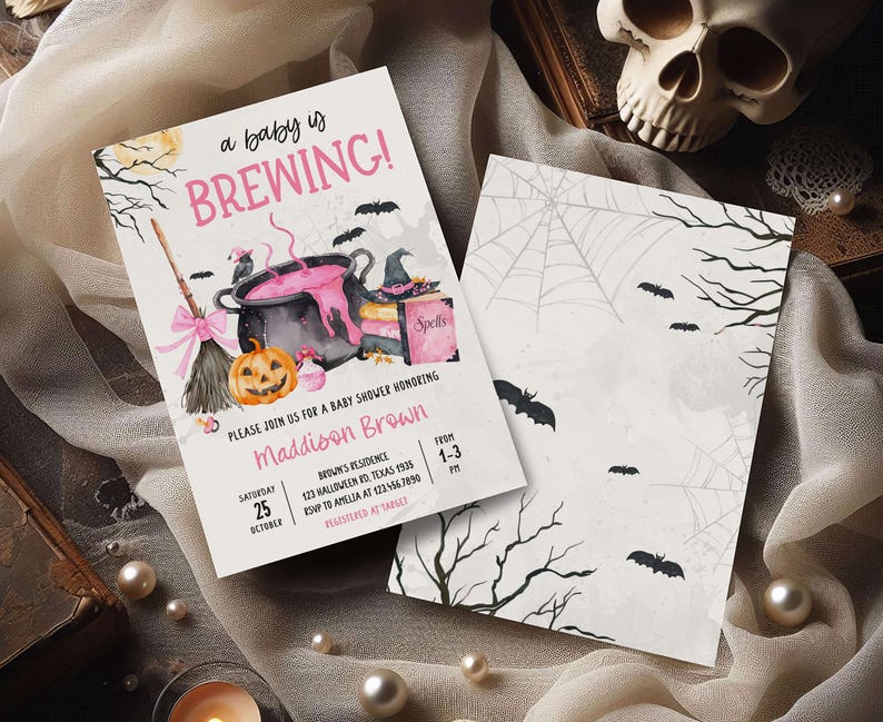 A Halloween-themed baby shower invitation featuring a witch's broom, a cauldron, and bats, along with a skull and spider web design.