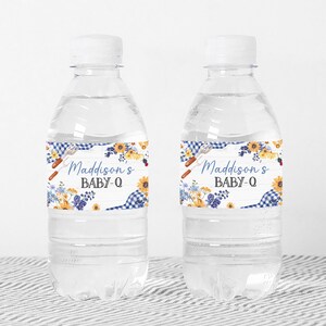 Puede incluir: Dos botellas de agua de pl&aacute;stico transparente con etiquetas de cuadros azules y blancos y flores. Las etiquetas dicen "Madisson's Baby-Q".