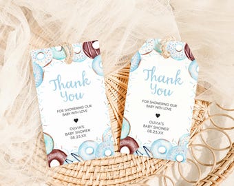 May include: Two blue and white donut-themed thank you tags for a baby shower. The text on the tags reads "Thank You" and includes the message "For showering our baby with love." The tags also include the name "Olivia's Baby Shower" and the date "08.23.XX".