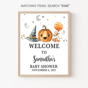 May include: A framed Halloween-themed baby shower sign. The watercolor illustration features a smiling pumpkin, witch hat, and ghost. The text reads "WELCOME TO Samantha's BABY SHOWER NOVEMBER 6, 2021".
