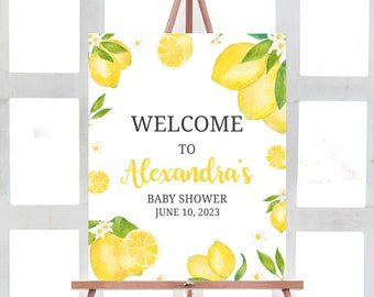 May include: Welcome to Alexandra's Baby Shower sign with a lemon theme. The sign features watercolor illustrations of lemons, leaves, and flowers in shades of yellow and green on a white background. The text "Welcome to Alexandra's Baby Shower June 10, 2023" is printed in black and yellow.