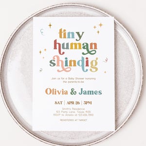 Könnte beinhalten: Eine farbenfrohe Babyparty-Einladung mit dem Text "tiny human shindig" in einer Retro-Schriftart. Die Einladung ist für Olivia & James und findet am Samstag, den 26. April um 15:00 Uhr statt. Die Veranstaltung findet in der Residenz Smith, 123 Party Lane, Texas 1935 statt. RSVP an Amelia unter 123 456 7890. Registriert bei Target.