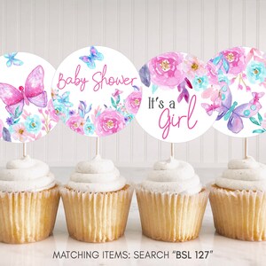 Pode incluir: Quatro toppers para cupcake com um design floral rosa e azul e borboletas. Os toppers dizem "Baby Shower" e "It's a Girl".