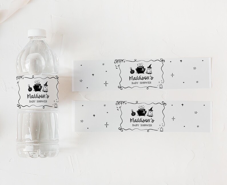 A clear plastic bottle and two white labels with black text and illustrations, likely for a baby shower, are placed on a white surface.