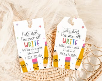 May include: Two white gift tags with the text "Let's start this year off WRITE" and "Wishing you a great school year!" are displayed. The tags feature illustrations of smiling pencils and stars. The tags are tied with twine.