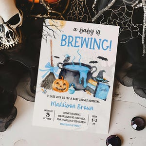 A Halloween-themed baby shower invitation featuring a skull, broom, cauldron, and pumpkins, with the text "a baby is BREWING!"