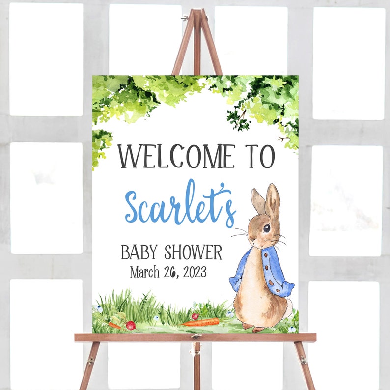 May include: Welcome to Scarlet's Baby Shower sign with a watercolor illustration of Peter Rabbit in a blue jacket standing in a green field with carrots and red berries. The date of the shower is March 26, 2023.