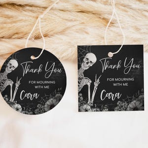 May include: Two black and white thank you tags featuring a skeleton graphic and floral accents. The text on the tags reads "Thank You for Mourning with Me Cara".