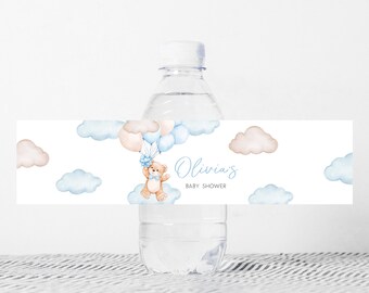 Może przedstawiać: Butelka wody z niestandardową etykietą z akwarelowym wzorem. Etykieta zawiera misia unoszącego się z balonami, chmurami i tekstem "Olivia's BABY SHOWER" w niebieskim skrypcie. Projekt ma miękkie niebieskie i beżowe kolory.