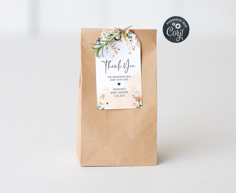Puede incluir: Una bolsa de papel marr&oacute;n con una etiqueta de agradecimiento floral adjunta. La etiqueta dice "Gracias" por duchar a nuestro beb&eacute; con amor, Baby Shower de Savannah, 5.20.2023.