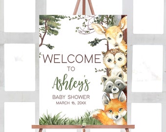 May include: Welcome to Ashley's Baby Shower sign with a watercolor illustration of woodland animals, including a deer, owl, raccoon, and fox. The sign is on a wooden easel and has a green and brown color scheme.