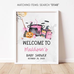 The image is a framed welcome sign for a baby shower, featuring Halloween-themed illustrations such as a cauldron, broomstick, jack-o-lantern, and bats.