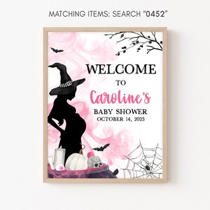 K&ouml;nnte beinhalten: Gerahmtes Babyparty-Schild mit Hexen-Thema. Auf dem Schild steht "Willkommen zu Carolines Babyparty am 14. Oktober 2023". Das Design umfasst eine Silhouette einer schwangeren Hexe, Flederm&auml;use, ein Spinnennetz und einen Kessel.