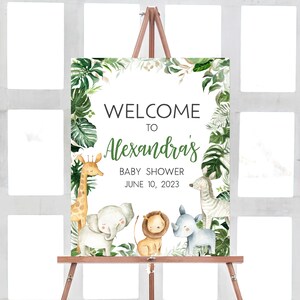 May include: Welcome to Alexandra's Baby Shower sign with a jungle theme. The sign features a giraffe, elephant, lion, zebra, and rhinoceros surrounded by green leaves.