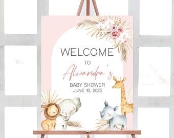 May include: A pink and white welcome sign for a baby shower with the text "Welcome to Alexandra's Baby Shower June 10, 2023". The sign features a watercolor illustration of a giraffe, elephant, lion, and rhino with a floral arrangement.
