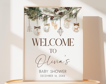 May include: A framed baby shower sign with the text "WELCOME TO Olivia's BABY SHOWER DECEMBER 14, 20XX." The sign features watercolor illustrations of baby-themed ornaments and pine branches.