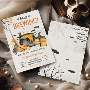 A Halloween-themed invitation for a baby shower, featuring a pot of bubbling soup, a jack-o-lantern, and bats, along with details about the event.