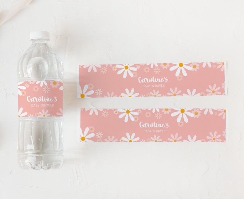 May include: Two pink and white daisy patterned labels with the text "Caroline's Baby Shower" printed on them. The labels are designed to wrap around a water bottle.