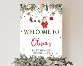 May include: A white sign on an easel with the words "Welcome to Olivia's Baby Shower" in green and red. The sign features a watercolor illustration of Christmas decorations and baby clothes. The date of the baby shower is December 14, 20XX.